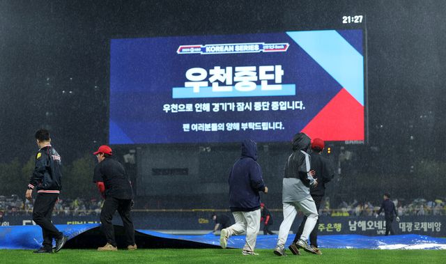 21일 광주 기아챔피언스필드에서 열린 2024 신한 SOL뱅크 KBO 포스트시즌 한국시리즈 1차전 삼성 라이온즈와 KIA 타이거즈의 경기. 6회초 강한 비로 경기가 잠시 중단되자 경기장 관계자들이 방수포를 경기장에 덮고 있다. /연합뉴스