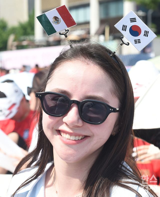2026 FIFA 북중미 월드컵 대한민국 대 멕시코의 본선 두번째 경기가 열린 19일 오전, 서울 광화문광장에서 한 멕시코 여성이 머리에 양국 국기를 꽂은채 KT 광화문 사옥 빌딩 벽면에 설치된 초대형 미디어 파사드 스크린을 보며 열띤 거리 응원을 펼치고 있다./ 이호형 기자 leemario@sporbiz.co.kr 2026.06.19