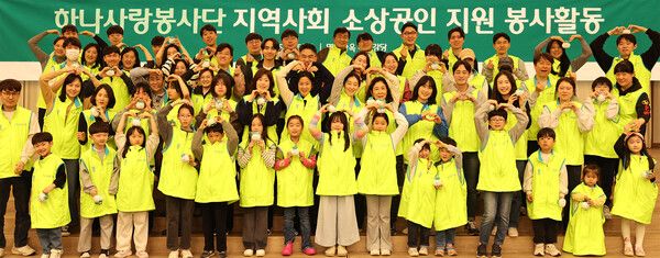 하나금융그룹은 지난 5일 지역사회 소상공인을 위해 그룹 임직원과 가족 100여 명이 참여하여 행복상자 만들기 및 거리환경 정비 봉사활동을 실시했다고 밝혔다. 이날 봉사활동에 참여한 임직원 및 가족들이 행복상자를 만들고 함께 모여 기념촬영을 하고 있다. [하나금융그룹]