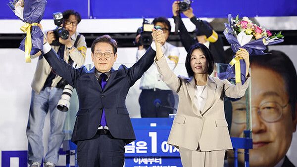 제21대 대통령 당선이 확실시되는 더불어민주당 이재명 대선 후보와 부인 김혜경 여사가 4일 서울 여의도 국회 인근에서 당 주최로 열린 국민개표방송 행사에 참석해 꽃다발을 받고서 시민들을 향해 두 팔을 들어올려 인사하고 있다. [KBS뉴스 갈무리]