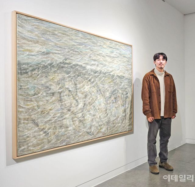 작가 우병윤이 서울 종로구 인사동길 선화랑 개인전 ‘중첩: 들떠 있는 풍경’에 건 자신의 작품 ‘율려 26-01-14’(2026, 130.3×162.0㎝) 곁에 섰다. 이번 개인전에 내놓은 ‘중첩’ ‘들떠 있는 풍경’ 외에 또 다른 연작인 ‘율려’는 전통적인 음악용어에서 작품명을 따온 만큼 좀 더 리드미컬한 흐름이 도드라진다. 산세가 잡히는 배경 위로 긁어낸 석고의 허연 흔적이 마치 거친 바람결처럼 덮였다(사진=오현주 문화전문기자).