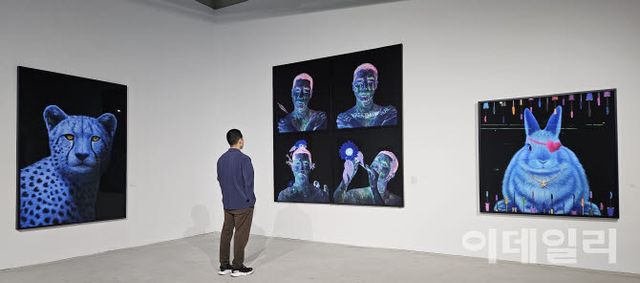 고상우 개인전 ‘너와 함께 쉬는 숨’ 전경. ‘자화상’ 연작 양쪽으로 ‘사라’(Sarah, 2026, 210×150㎝·왼쪽)와 ‘사라진 감각’(Lost Senses, 2026, 150×150㎝)이 보인다. 화장품 임상시험에 나섰다가 한쪽 눈의 시력을 잃은 토끼는 알록달록한 ‘마스카라 창살’ 안에 갇혀 있다(사진=오현주 문화전문기자).