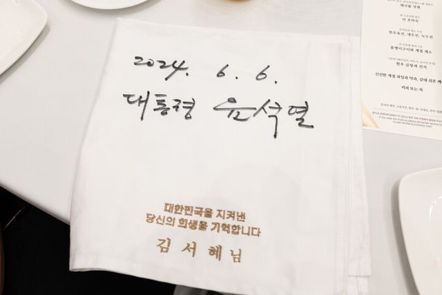 윤석열 대통령이 6일 청와대 영빈관에서 열린 국가유공자 및 보훈가족 초청 오찬에서 참석자들의 요청으로 참석자들의 이름이 자수로 새겨진 냅킨에 사인을 했다. [사진=대통령실]