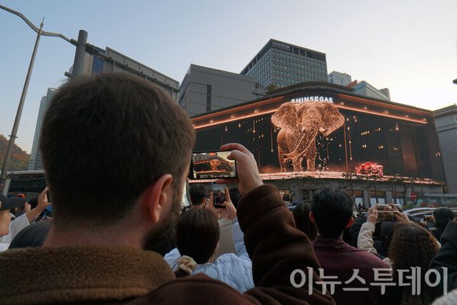서울 중구 신세계백화점이 본점에서 한 외국인 관광객이 외벽에 설치된 ‘신세계스퀘어’를 통해 재생되는 ‘시간을 잇는 마법의 세계’ 크리스마스 영상을 휴대폰으로 촬영하고 있다. [사진=이뉴스투데이DB]