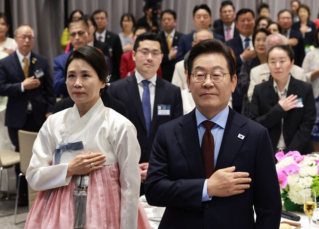 이재명&nbsp;대통령과 김혜경 여사가 24일(현지시간) 미국 워싱턴DC의 한 호텔에서 열린 동포 만찬 간담회에서 국기에 경례하고 있다. [사진=연합뉴스]