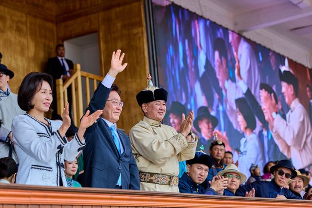 이재명 대통령이 11일(현지 시각) 몽골 울란바타르 국립체육경기장에서 오흐나 후렐수흐 대통령과 나담축제 개막식 관람 중 손을 흔들고 있다. 왼쪽은 김혜경 여사. [사진=연합뉴스]