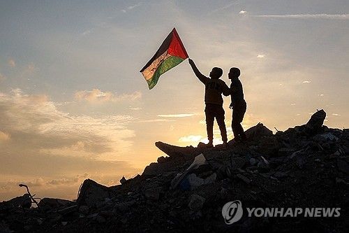 17일(현지시간) 가자지구 난민촌 잔해더미 위에서 팔레스타인 국기를 흔드는 소년