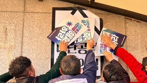 국민의힘 당원협의회 사무실 외벽에 스티커 붙이는 민주노총 경남본부 소속 회원들