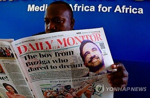 우간다 출신 맘다니 당선 소식이 실린 신문을 보는 우간다 남성 
