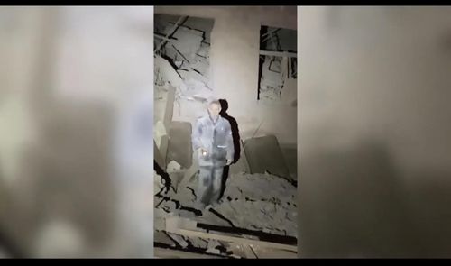 무너진 학교 잔해 속에 서 있는 남성의 모습