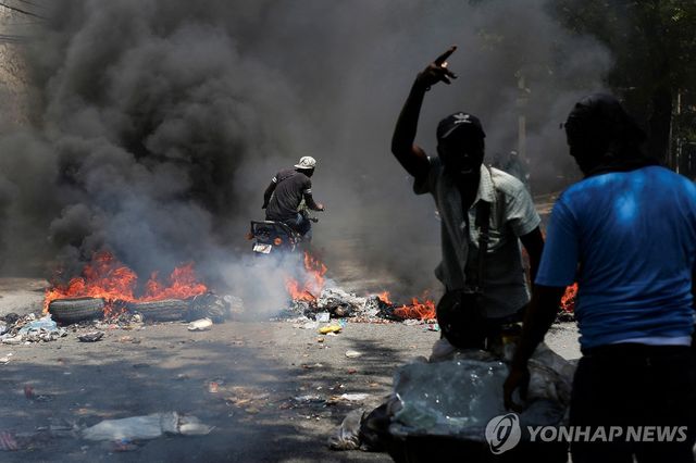 지난 19일(현지시간) 도로 위 불타는 바리케이드를 지나가는 아이티 주민