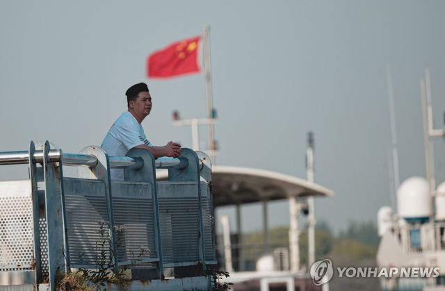 중국 상하이 컨테이너 터미널에서 선박을 바라보고 있는 한 남성 뒤로 중국 국기인 오성홍기가 휘날리는 모습.