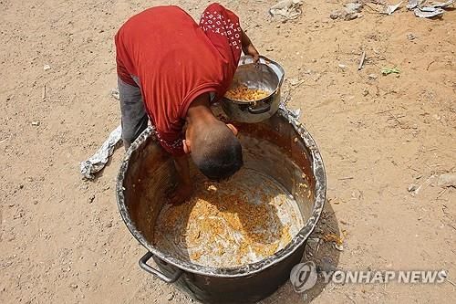 가자지구의 한 소년이 자선단체의 냄비 바닥에 남은 음식을 긁어 모으고 있다. 