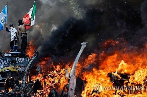 LA에서 차량이 불타고 있는 가운데 깃발을 든 불법이민자 단속 반대 시위대 