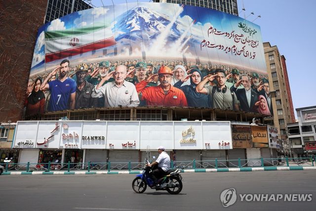 22일(현지시간) "우리는 모두 이란의 군인이다"라 쓰인 광고판을 지나는 테헤란 시민
