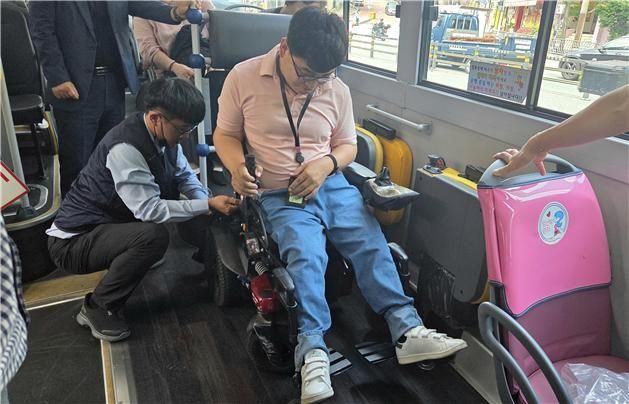 저상버스 운전기사가 휠체어에 좌석 고정벨트를 채우고 있다