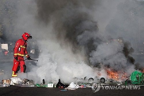 파리의 한 고등학교 앞에서 소방관이 불타는 쓰레기통과 물건들을 진화하고 있다. 