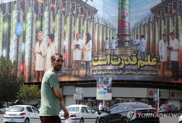 지난달 29일 이란 테헤란의 엥헬랍 광장에서 핵 원심분리기 사진과 함께 '과학이 힘이다'라고 적힌 광고판 앞을 한 행인이 지나가고 있다. [EPA=연합뉴스 자료사진]