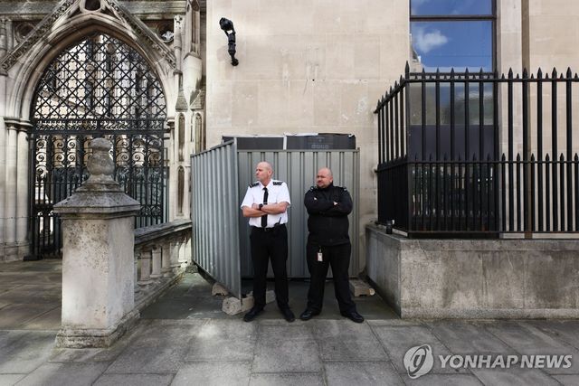 8일(현지시간) 영국 런던 왕립법원 외벽에 그려진 뱅크시의 벽화를 가린 차단막 앞에 보안 요원들이 서 있다.[로이터=연합뉴스. 재판매 및 DB 금지]