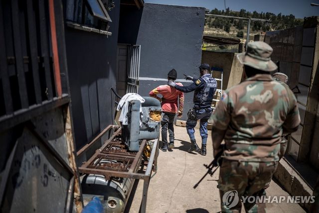 11일(현지시간) 남아프리카공화국 요하네스버그 리버리 지역에서 군인이 서 있는 가운데 경찰이 한 남성을 붙잡고 있다. [AFP=연합뉴스 자료사진. 재판매 및 DB 금지]