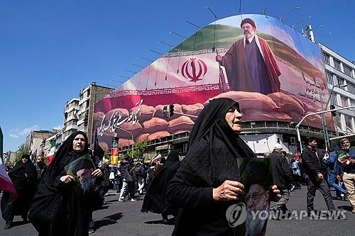 이란 테헤란에서 하메네이 사망 40일을 기리는 행사가 열린 가운데, 여성들이 현 최고지도자 모즈타바 하메네이의 모습이 담긴 대형 벽화 앞을 지나고 있다. [AP 연합뉴스]