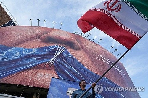 이란 수도 테헤란의 한 광장에서 호르무즈 해협과 입이 꿰매진 도널드 트럼프 미국 대통령의 모습이 그려진 광고판 아래에서 한 남성이 이란 국기를 흔들고 있다. [AP 연합뉴스 자료사진. 재판매 및 DB 금지]