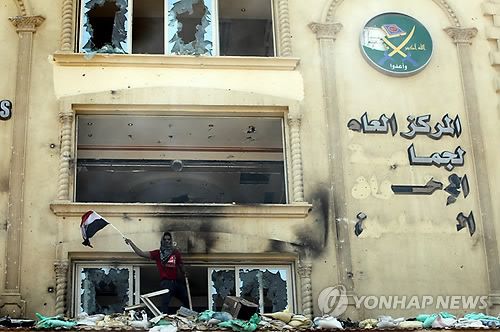 2013년 7월 1일 카이로 소재 무슬림형제단 본부가 시위대 공격을 받은 뒤 한 시민이 이집트 국기를 흔들고 있다. 같은 해 9월 카이로 법원은 무슬림형제단 활동을 금지하고 자산 몰수를 명령했다. [EPA 연합뉴스 자료사진]