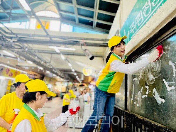 시장 유리를 닦으며 환한 미소를 전하고 있는 마산지부 봉사자들 모습. /사진-신천지자원봉사단 마산지부