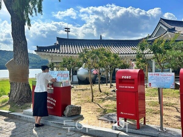 보문관광단지를 찾은 여행객이 보문호반광장 앞에 설치된 느린우체통 옆에서 보내려는 엽서 작성하고 있다./사진=경북문화관광공사