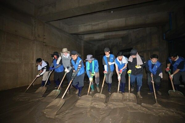 수해를 입은 지하 시설에서 '바르게살기운동 옥포1동위원회' 봉사자들이 일렬로 늘어서서 바닥에 쌓인 두꺼운 토사를 치우고 있다.