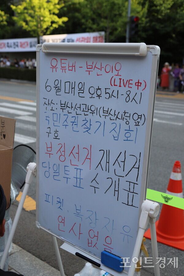 지난 12일 연제구 부산시선관위 앞 시위 현장에 설치된 화이트보드 안내판에 집회 시간(오후 5시~8시)과 주요 구호, 그리고 언론의 왜곡 프레임을 경계하기 위한 ‘복장 자유, 연사 없음’이라는 문구가 적혀 있다. (사진=윤선영) ⓒ포인트경제
