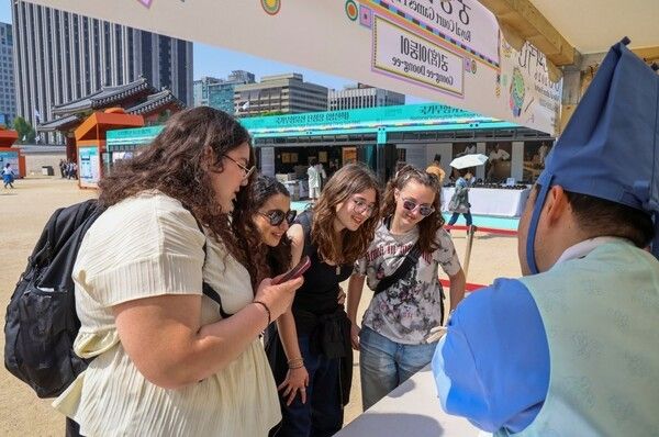 경복궁 궁중놀이방 - 궁(宮)이둥이와 외국인 관광객의 만남2026 봄 궁중문화축전이 한창인 경복궁 흥례문 광장 ‘궁중놀이방’ 부스에서 외국인 관람객들이 자원활동가 ‘궁(宮)이둥이’와 함께 미션 카드를 살펴보며 즐거워하고 있다. 궁중놀이방은 ‘궁이둥이를 이겨라’, ‘궁퀴즈’, ‘궁셀샷’ 등 자원활동가가 직접 기획·운영하는 소규모 체험·이벤트 공간이다. 사진=국가유산진흥원