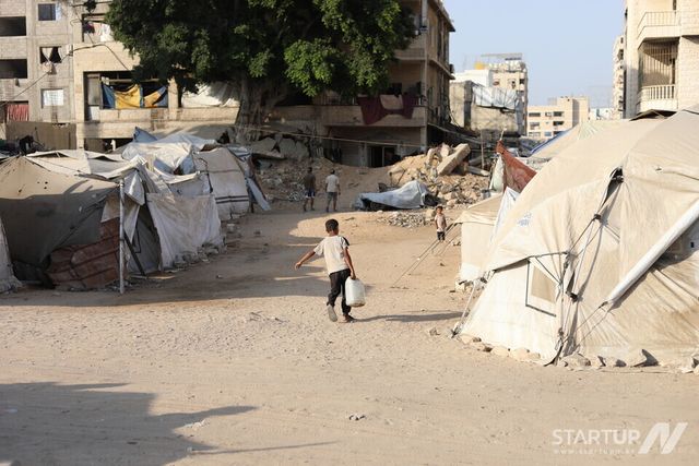 무거운 물통을 들고 가족들이 있는 텐트로 돌아가고 있는 아동. 2025년 8월 (사진 = 국경없는의사회 제공)