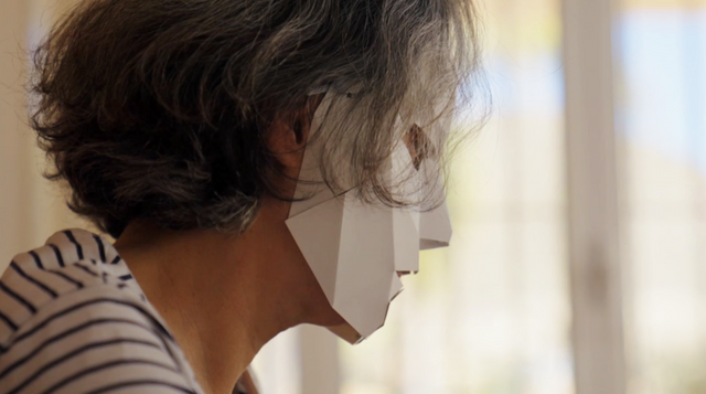 종이 마스크를 쓰고 책상 앞에 앉아 있는 마리아의 모습