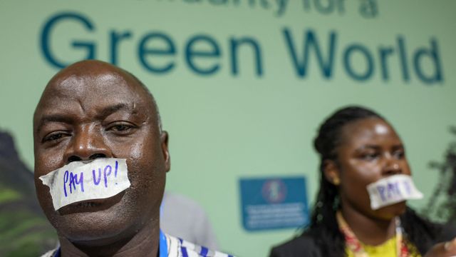 아제르바이잔 바쿠에서 열린 COP29에서 두 사람이 "녹색 세계를 위한 연대"라고 적힌 벽 앞에서 "더 많이 내라!"고 적힌 테이프를 입에 붙이고 있다