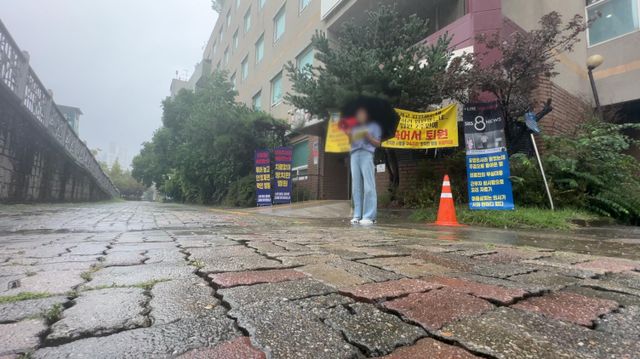 비가 내리는 날, 유족이 병원 앞에서 우산을 들고 1인 시위를 하고 있다. 