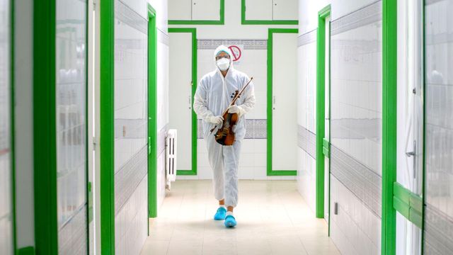 보호 장비를 착용한 의료 종사자가 바이올린을 들고 있는 모습