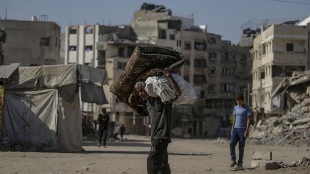 어깨에 짐을 지고 무너진 건물 잔해가 널린 가자 시티 거리를 걷는 남성의 모습