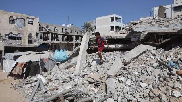 2025년 10월 8일 가자지구 칸유니스의 한 임시 거주시설에 머무는 팔레스타인 어린이가 무너진 건물 잔해 속에서 무언가를 찾고 있다.