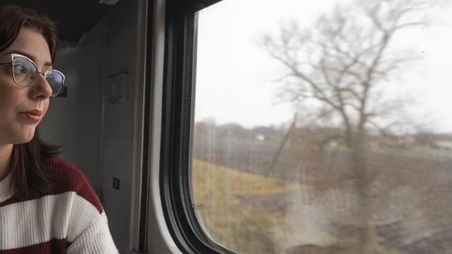 안경을 쓴 여성이 열차 창밖을 바라보고 있다. 