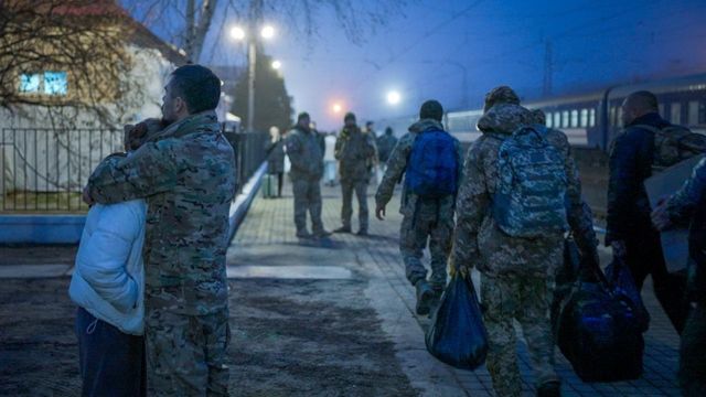군인들이 지나가는 가운데 연인들이 기차역 승강장에서 서로를 끌어안고 있다. 