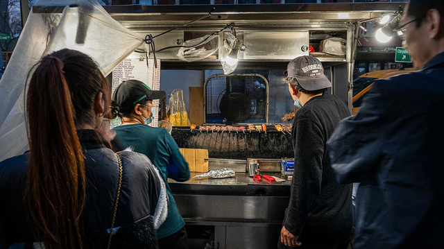 노점 앞에 사람들이 줄을 서 있고, 가게 안에서는 직원들이 꼬치를 굽고 있다.