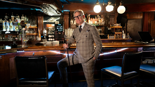 양복을 입은 중년의 남성이 바 안에서 카운터 앞에 서 있다.