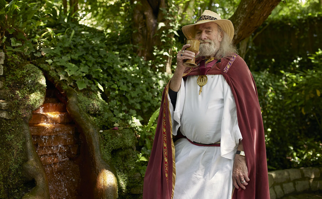 전통 의상을 입은 한 남성이 잔을 들고 미소를 짓고 있다.