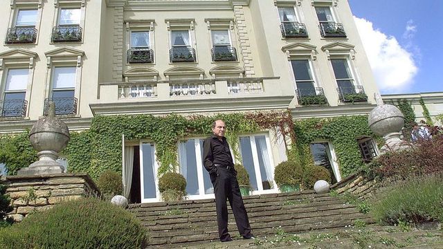 검은 옷을 입은 한 남성이 주택 앞 계단에 서 있다.