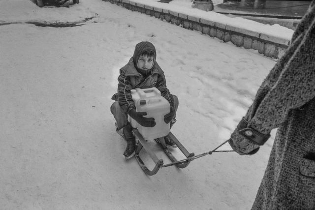겨울에 물통을 안고 썰매를 타는 어린 아이의 흑백 사진