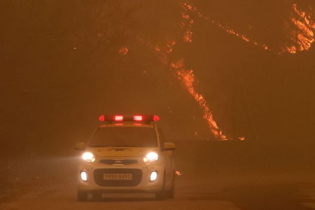 25일 오후 경북 안동시 길안면 백자리에 강풍이 불어 주변 산이 화염에 휩싸인 가운데 소방관계자들이 대피 명령이 내려진 마을 곳곳을 순찰하고 있다