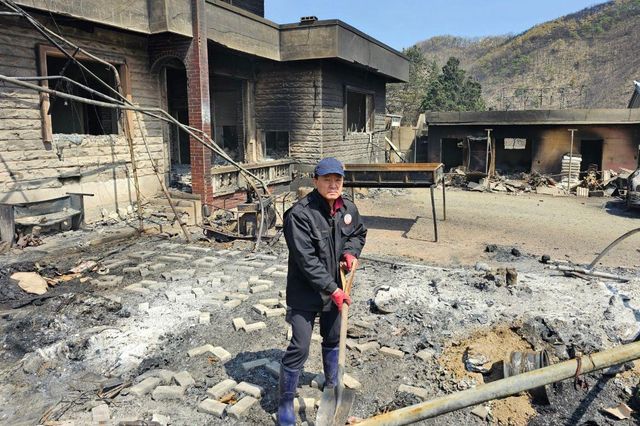 권오석 씨가 삽을 들고 화재 피해로 무너지고 그을린 집 앞에 잔해를 치우고 있다