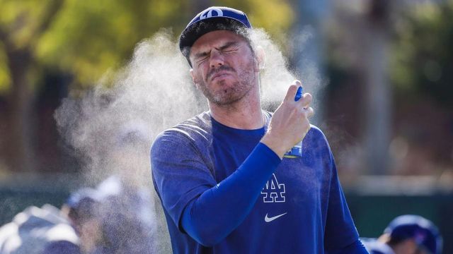 파란색 긴팔 티셔츠를 입고 스프레이형 선크림을 뿌리고 있는 남자