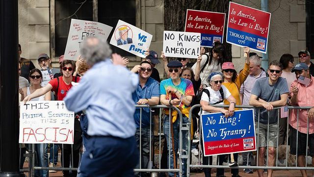 시위대가 금속 바리케이드 뒤에 서서 '미국에선 법이 곧 왕이다'와 '왕과 독재에 반대한다'라고 적힌 팻말을 들고 있다
